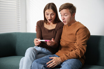 Emotional couple with pregnancy test on sofa at home