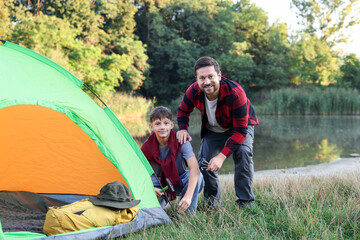 Happy father and son setting up camping tent near river outdoors