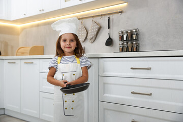 Choice of profession. Little girl with frying pan pretending to be chef in kitchen