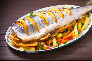 Roasted salmon with lemon, oranges and herbs served with vegetables on oval plate