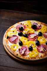 Pizza with salami, mozzarella cheese, black olives and pepper. Rustic wooden background. Soft focus. Copy space.	