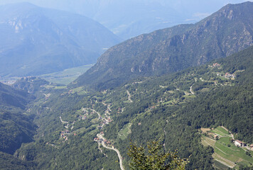 Aerial view of a valley between mountains with many green trees in the Italian Alps