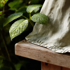Dew-covered garden leaves beside draped linen on a wooden bench. AI generative