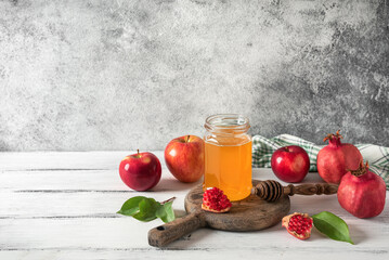 Jar of honey with a wooden dipper, apples and pomegranates on a light rustic background.