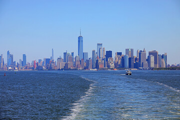 skyline of the island of Manhattan with very high skyscrapers and the wake of a ship on the ocean waters during the day