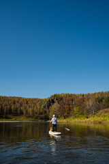 Fototapeta premium Enjoy thrilling standup paddleboarding on a beautiful autumn day, surrounded by stunning landscapes and calming lake reflections, offering a perfect mix of relaxation and adventure