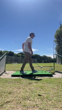 A man is walking on a golf course with a golf club in his hand. The sky is clear and bright, and the grass is green. The man is focused on his game, and the scene suggests a sense of calm