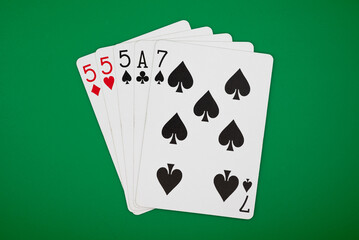 Playing cards showing three of a kind poker hand on a green background, symbolizing gambling, poker, and the risks of casino games.