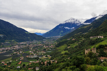 Panorama with castle Schloss Brunnenburg, snowcapped mountain summit Cima di Tel (Zielspitze) and valley Etschtal seen from Tirol (Dorf Tirol) on a cloudy day in autumn in South Tyrol, Italy