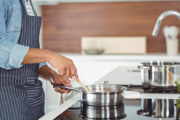 Obraz na płótnie Canvas African American man in apron stirring skillet with spatula at cooktop in kitchen, copy space Obraz na płótnie Canvas African American man in apron stirring skillet with spatula at cooktop in kitchen, copy space