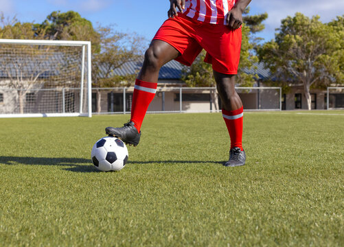 African American male controlling soccer ball on pitch in striped jersey and cleats beside goalpost - Powered by Adobe