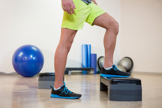 Male exerciser performing step-up exercise on platform in gym with stability ball and Bosu balls