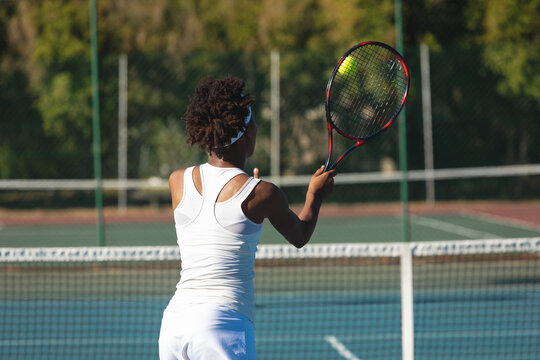African American woman tennis player swinging racket hitting yellow ball behind net on court