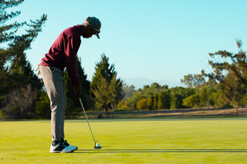 African American man lining up putt on putting green holding putter and ball, copy space