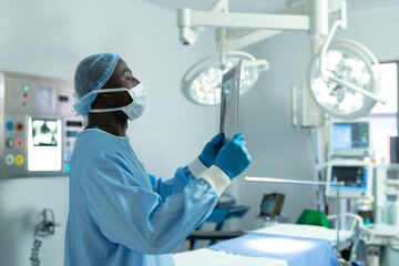 African American male adult surgeon examining X-ray film under LED lamps in hospital OR, copy space