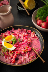 A colorful bowl of beet soup features chopped vegetables, sliced eggs, and fresh herbs. The setting includes a jug of cream, a lemon, and radishes, creating a cozy atmosphere