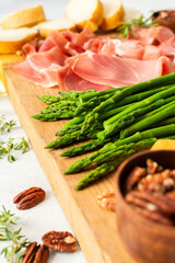 This charcuterie board displays a variety of cured meats, cheeses, fresh asparagus, and nuts arranged neatly, inviting people to enjoy a delicious meal or snack together