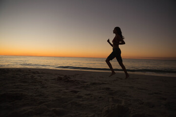 Adult female running barefoot on sandy shoreline at dusk with gentle waves and horizon, copy space