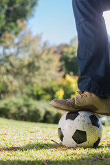 Lower legs in dark blue jeans and tan sneakers pressing soccer ball on sunlit grassy field