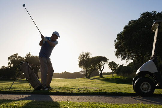 Senior golfer swinging driver club at tee box on golf course aiming golf ball, copy space - Powered by Adobe