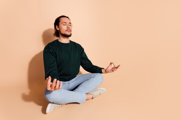 Young man in casual attire meditating against beige background for relaxation and mindfulness concept