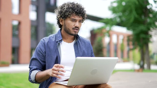 Worried businessman having problems with software or service on laptop computer sitting on a bench near a office building. Frustrated disappointed man complains about bad internet connection. Close up