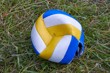 One deflated volleyball ball lying on green grass.