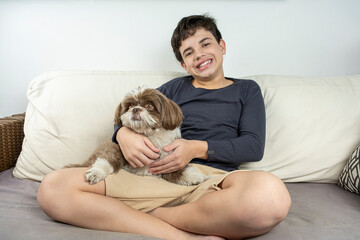 Smiling 12 year old Brazilian teenager on the sofa next to his dog.