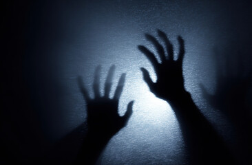Silhouetted hands reaching out against textured, illuminated background create mysterious and eerie atmosphere