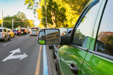 Green car parked by urban street with heavy city traffic and sunlight reflections. Concept of traffic, driving and car transportation