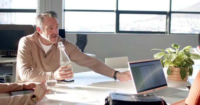 Hispanic woman starting chat in office, senior man pouring water for arriving colleague leaning