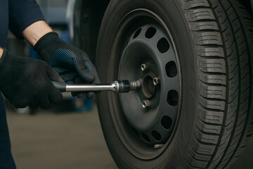 Mechanic tightening car wheel bolts with torque wrench during tire replacement in auto repair shop, concept of maintenance, automobile service, garage, and professional mechanic work