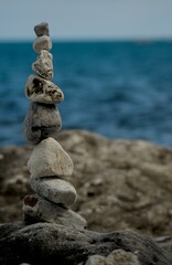 A tranquil scene featuring a balanced stack of smooth stones on a rocky shore, with the blue Adriatic Sea in the background. Captured in Portonovo, Marche, Italy, this image symbolizes balance