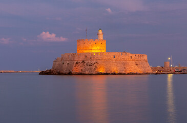 Illuminated Fort Saint Nicholas in Mandraki harbor at sunset in Rhodes Greece