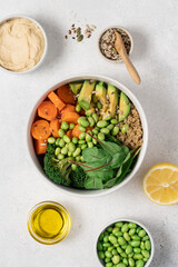 White Bowl with with Healthy Quinoa Salad, Edamame Beans, Broccoli, Carrot, Lettuce Leaves and Avocado Surrounded by Ingredients  on Light Background, Clean Eating Concept