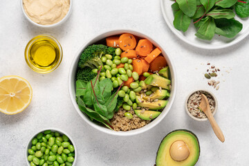 White Bowl with with Healthy Quinoa Salad, Edamame Beans, Broccoli, Carrot, Lettuce Leaves and Avocado Surrounded by Ingredients  on Light Background, Clean Eating Concept