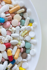 A white plate tablets pills capsules of different shapes, sizes and colors. macro view. beige table background.