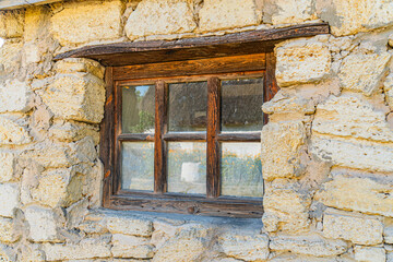 Close-up of an aged, stone window in a Central European village Divided into three panes, set in weathered wood frame Visible signs of repair and aging on the wall Subdued earthy tones under natur