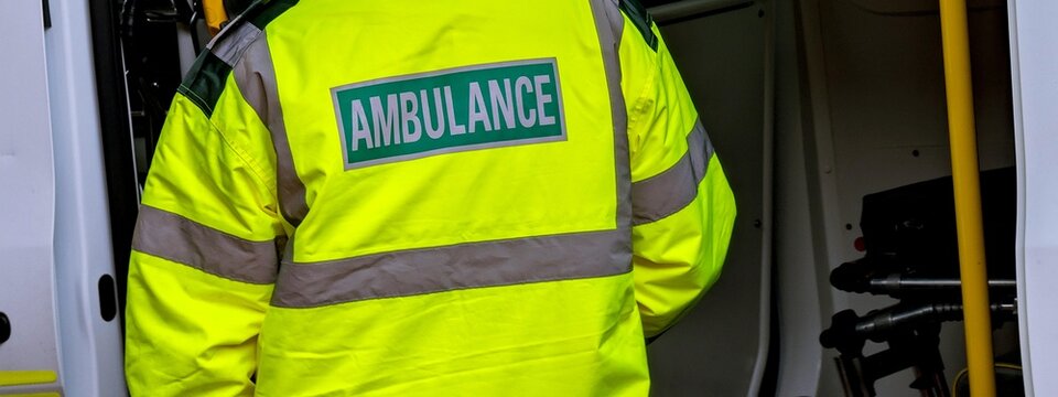 A close-up of an ambulance worker's high-visibility jacket with "Ambulance" text, a concept for emergency and medical services