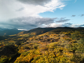 Autumn mountains with colorful forest and golden foliage under dramatic cloudy sky, wide seasonal landscape view