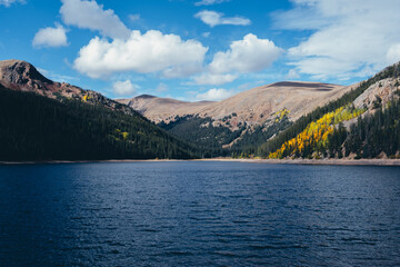 Mountain lake with deep blue water surrounded by forest and autumn foliage under cloudy sky, scenic seasonal landscape