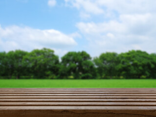 Wooden table in a sunny park with green trees and blue sky in the background during the day