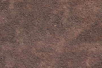 Natural reddish-brown dirt surface with various small pebbles in bright daylight