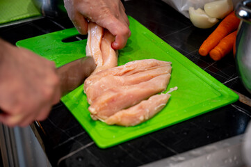 Slicing Chicken Fillet into Pieces on Plastic Cutting Board