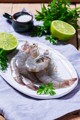 Fresh shrimp, lime, salt, and parsley on a ceramic plate on a wooden table.