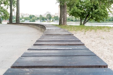 Tranquil seaside park with a curved concrete path, stone border, soft shadows, warm glow, muted browns, green background, recent rainfall, naturalistic style, first-person perspective
