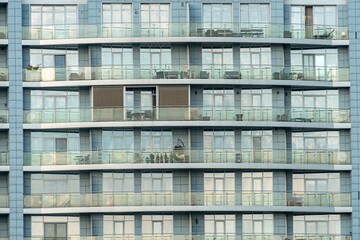 Obraz premium A multi-story, curved modern European building in urban setting Gray and blue tones, dark lower section, light upper part Transparent glass balcony railings, furnished balconies suggest residential
