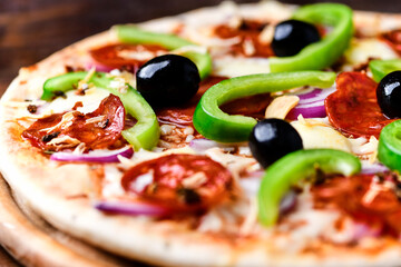 Pizza with chorizo ​​sausage, mozzarella cheese, green pepper and black olives. Rustic wooden background. Soft focus.	