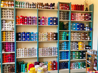 Colorful yarn store, blue and white shelved, array of rainbow-colored yarns with diverse patterns, depth from foreground items, natural lighting casting soft shadows