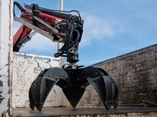 Industrial hydraulic grapple claw attachment inside truck container, showing black jaws, hoses, and...